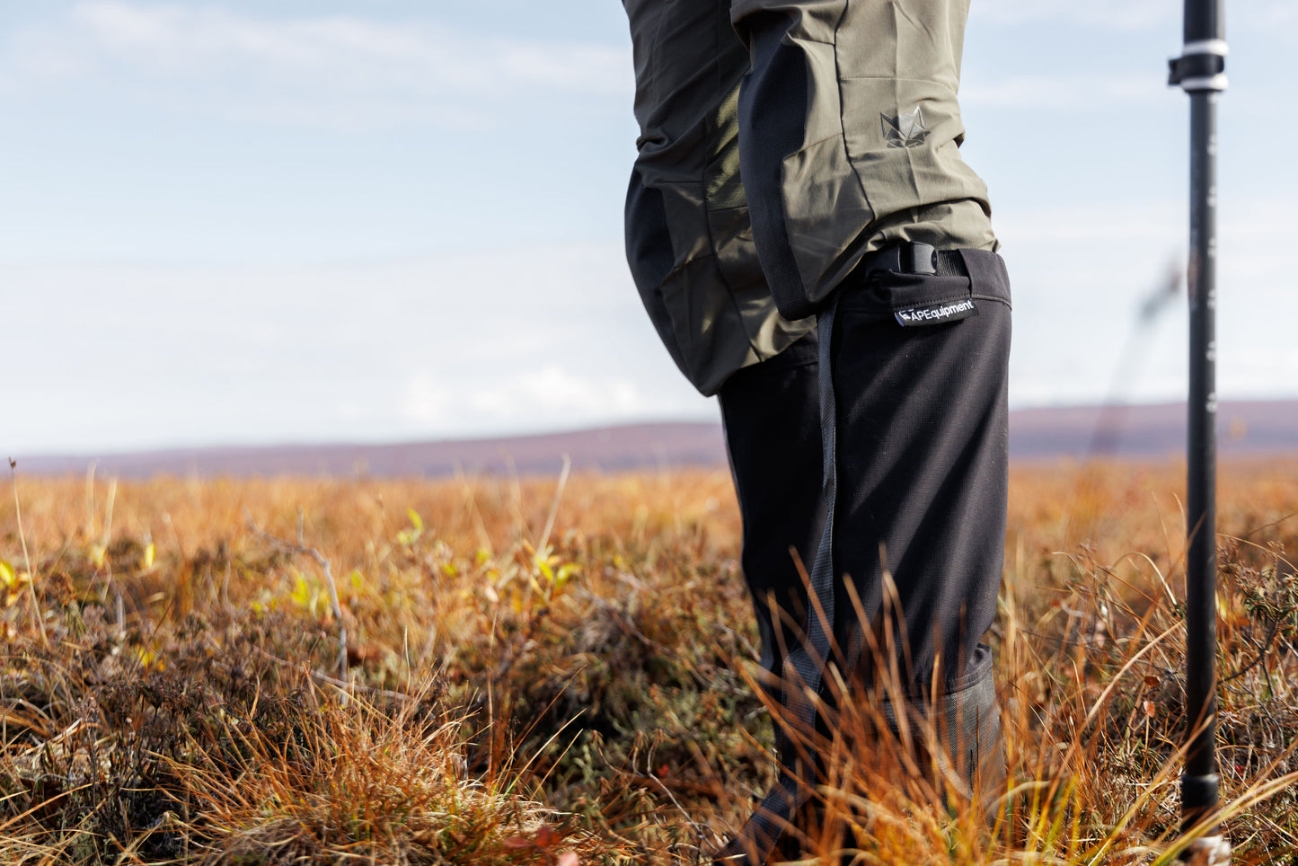 Person wearing outdoor gear with a hiking pole in a field