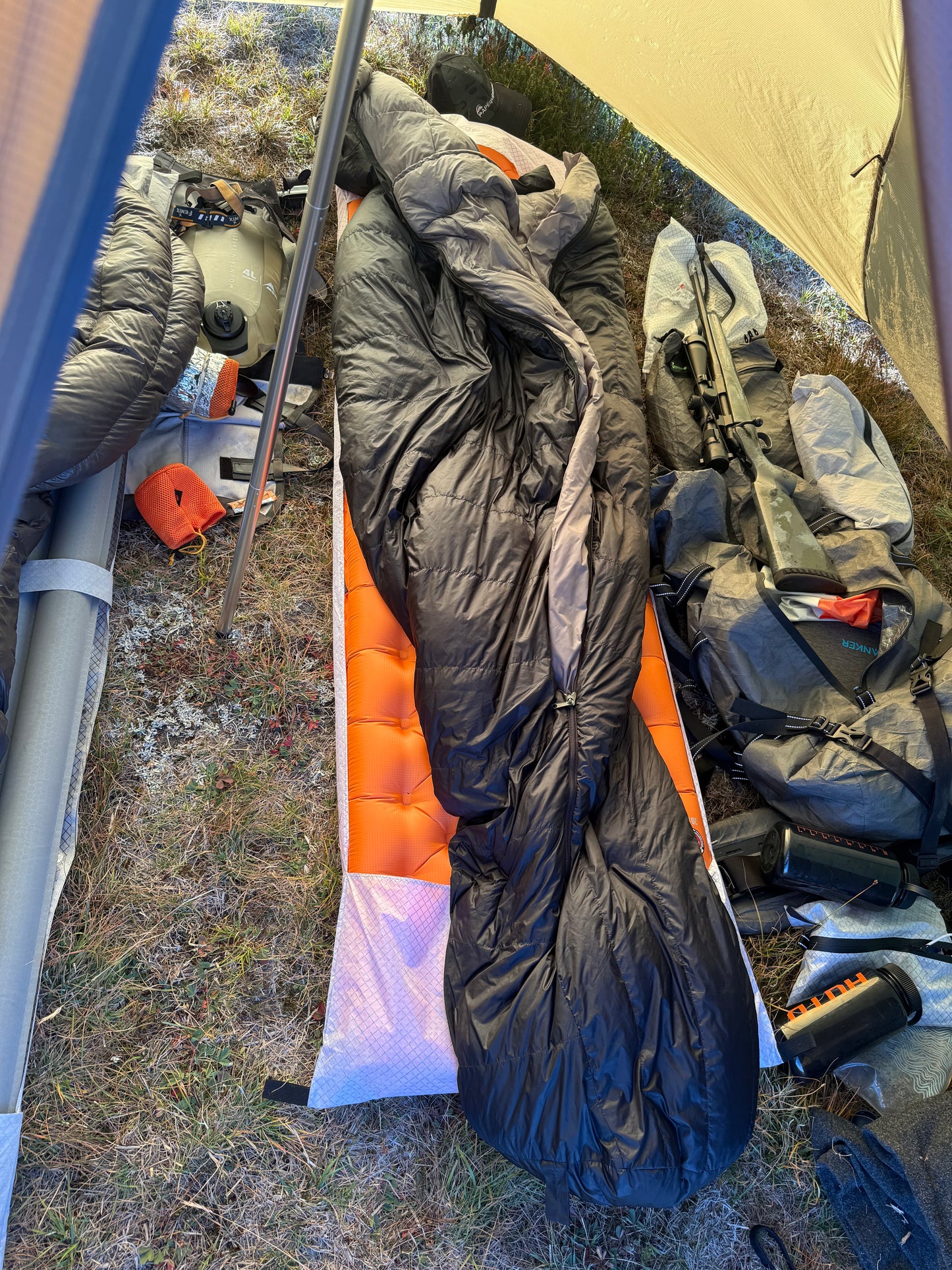 Sleeping bags and camping gear on the ground with a tent in the background