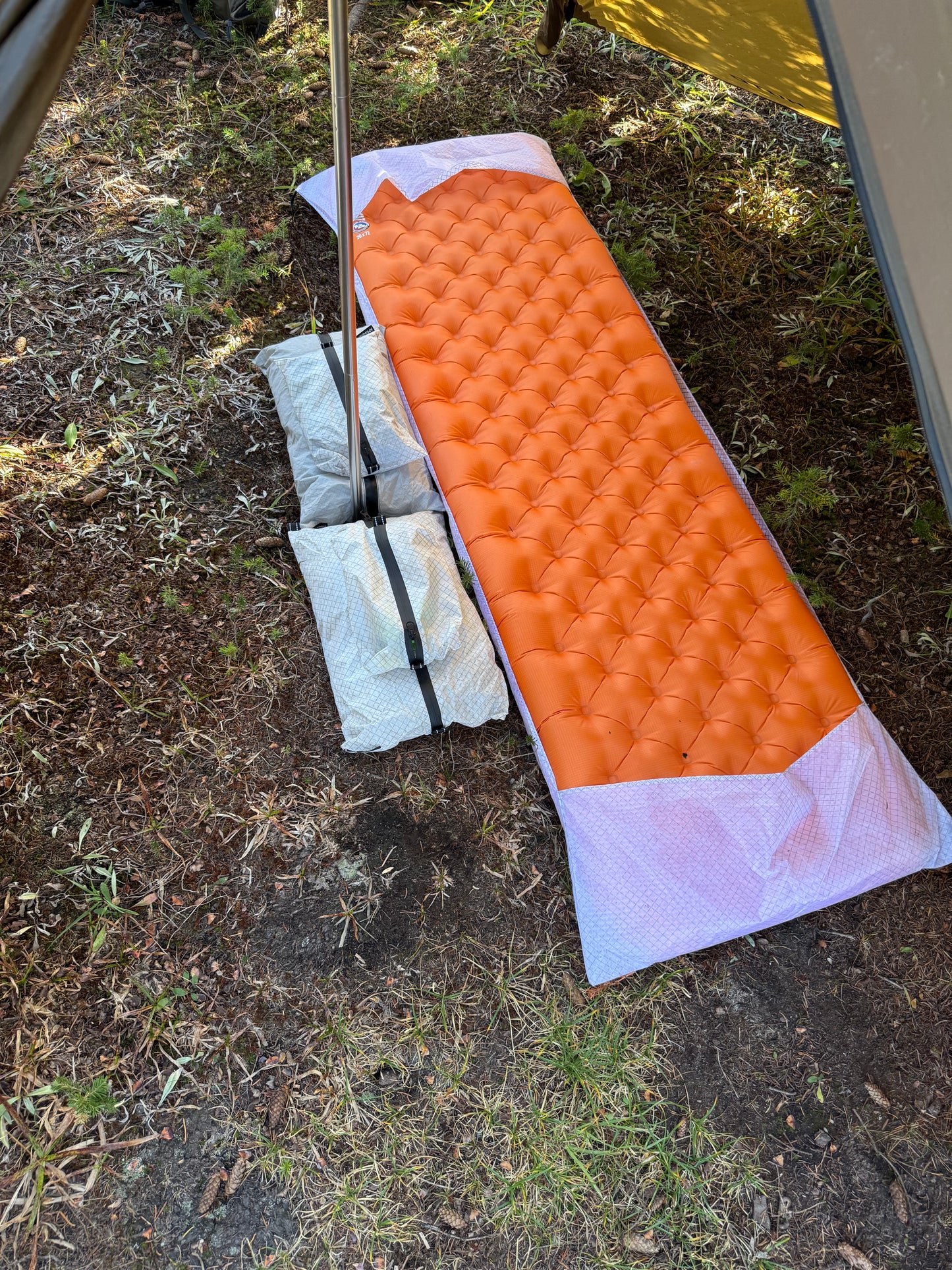 Orange camping mattress on the ground with a tent partially visible