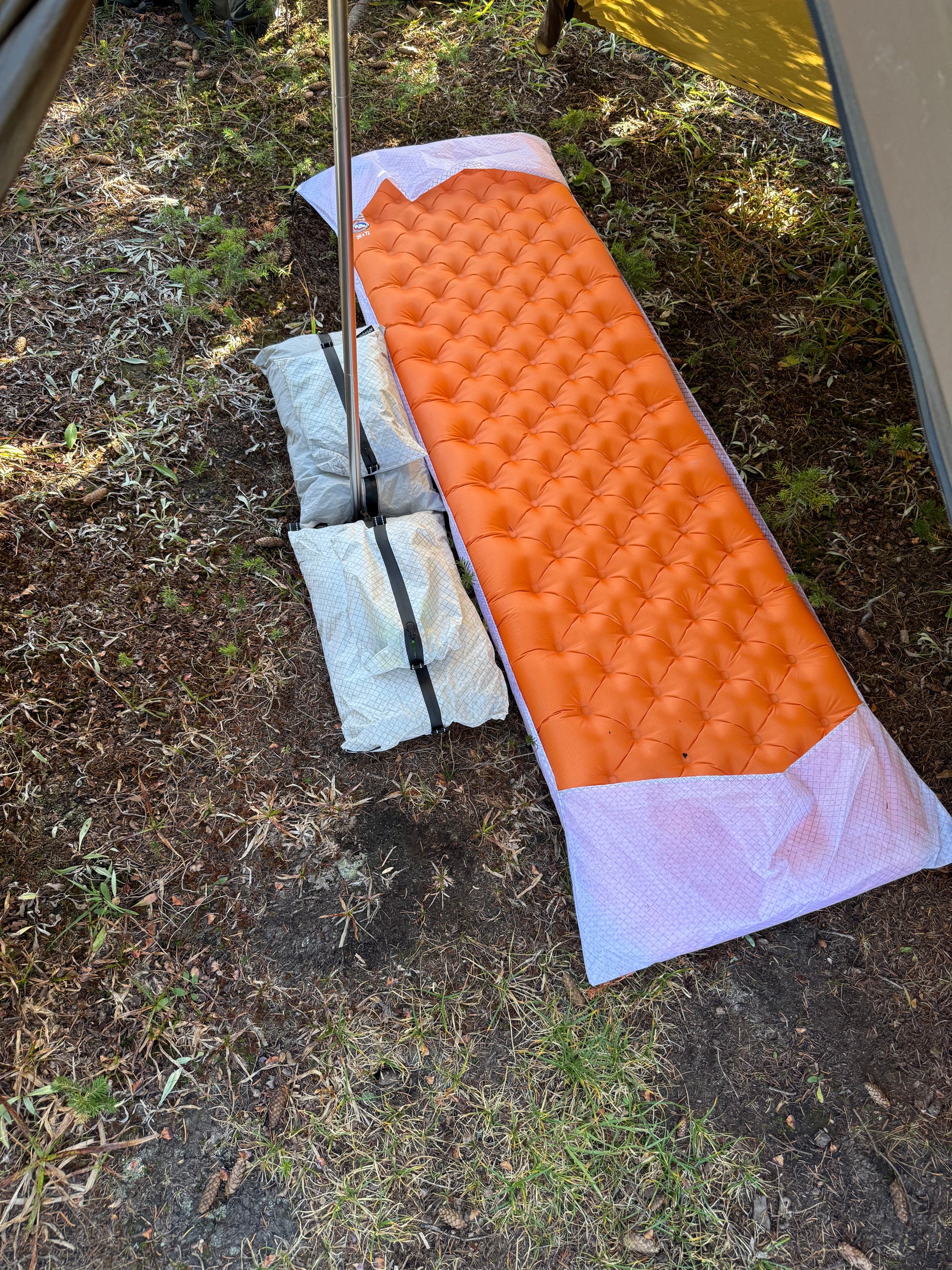 Orange camping mattress on the ground with a tent partially visible