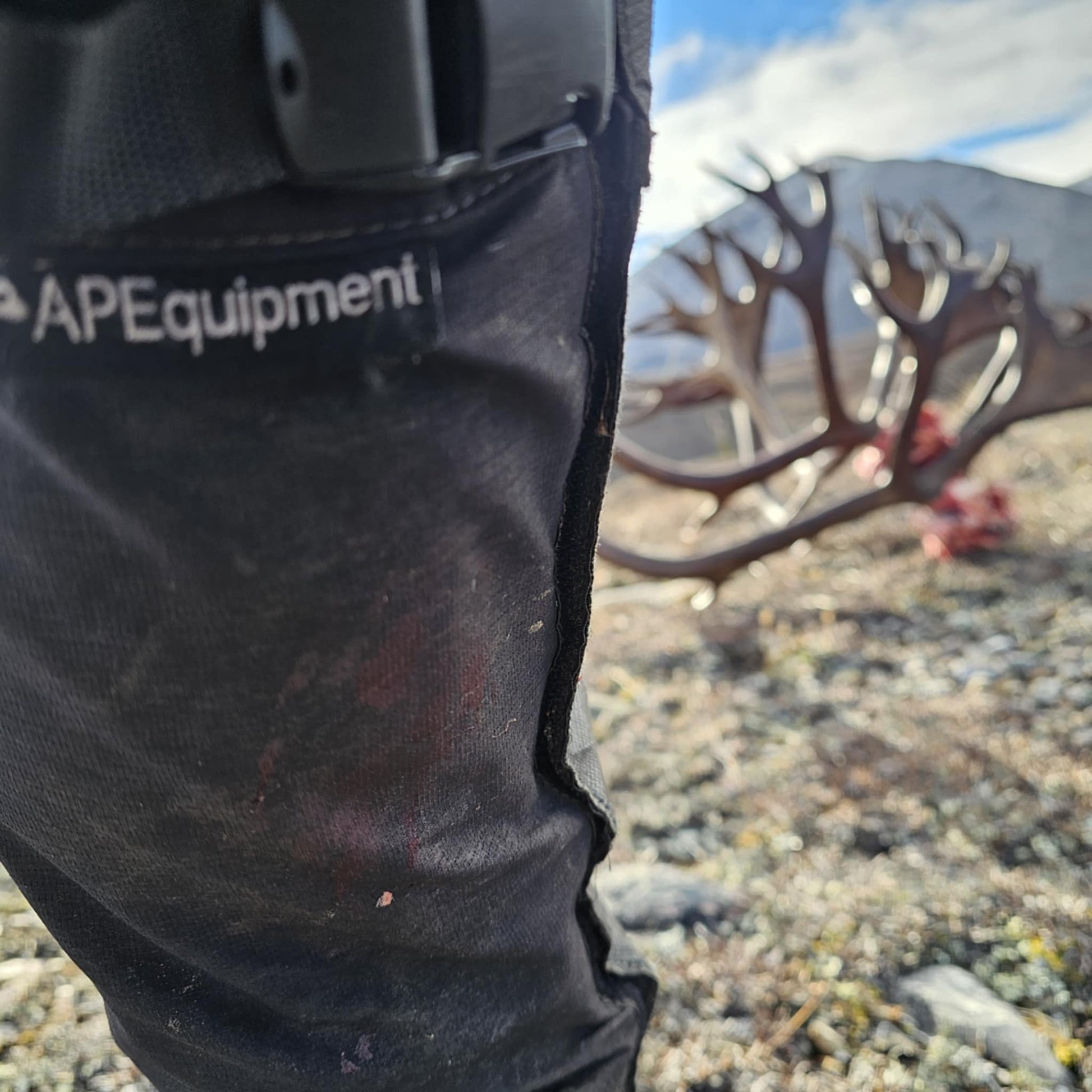 Close-up of black pants with 'APEquipment' branding, blurred natural background