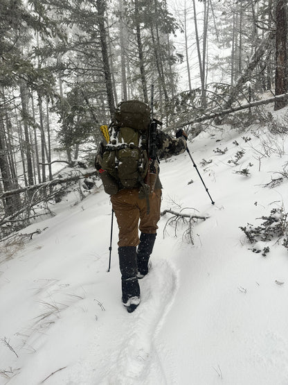Person in winter gear standing on a snow-covered ground with trees in the background